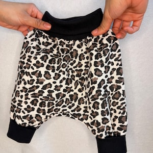 Op de afbeelding: Babybroek met een zwart, wit en bruin luipaardpatroon. Het kledingstuk is voorzien van een brede zwarte elastische tailleband en bijpassende zwarte geribbelde boorden bij de enkels voor een goede pasvorm.