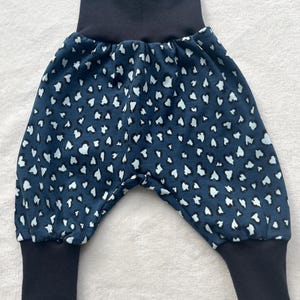 Op de afbeelding: Marineblauwe babybroek met een wit en lichtblauw hartvormig patroon. De broek heeft een hoge, donkerblauwe tailleband en bijpassende manchetten aan de enkels. De stof ziet er zacht en comfortabel uit, geschikt voor baby's en peuters.