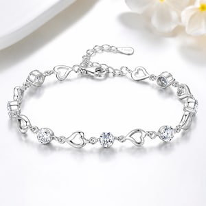 May include: A silver-toned chain bracelet featuring alternating open heart-shaped links and round, clear, faceted stones. The bracelet includes a lobster claw clasp and an adjustable extender chain with a small tag stamped with the text S925.
