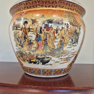 May include: A ceramic planter featuring a hand-painted scene of four figures in traditional attire within a landscape. The rim and base are decorated with intricate geometric patterns in red, gold, and blue. The central artwork depicts people.