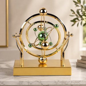 May include: A kinetic desk sculpture featuring a gold-toned metal frame with rotating rings and spheres. The center contains a large green metallic sphere surrounded by smaller green and gold spheres, all mounted on a rectangular gold base.