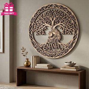 Op de afbeelding: Houten wandkunst met een boomontwerp, een moeder en kind, en het woord "MAMA". Het kunstwerk is cirkelvormig met ingewikkelde uitgesneden details en een natuurlijke houten afwerking. Het wordt weergegeven op een neutraal gekleurde muur.