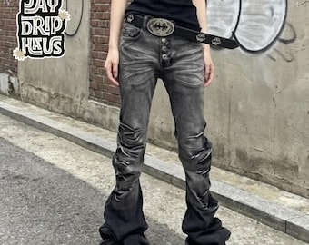 May include: Black denim jeans featuring a faded wash, a button-fly closure, and gathered, ruched fabric along the lower legs. The jeans are paired with a black belt featuring a large, ornate silver-tone buckle. The text JAY DRIP HAUS is visible.