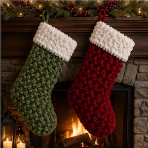 Puede incluir: Dos calcetines navideños de punto grueso, uno en verde bosque y otro en rojo intenso, ambos con un puño grueso y texturizado de color crema y un lazo para colgar a juego. Los calcetines presentan un denso patrón de punto en relieve.