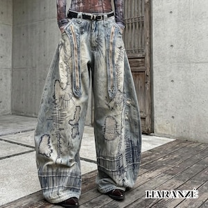 May include: Faded blue denim jeans with a wide leg design. The jeans feature decorative stitching, distressed patches, and two vertical zippers. The brand name "HARANZE" is printed in white on the lower right corner.