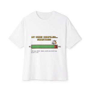 May include: White t-shirt featuring the text "MY CODE COMPILES... SOMETIMES" in a pixelated font. Below the text is a progress bar graphic with a cartoon character and the text "CRITICAL ERROR: SNACK_OVERFLOW EXCEPTION, RETRY? (Y/N)".