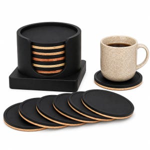 May include: A set of round drink coasters with black tops and layered wood edges, stacked inside a black cylindrical holder. One coaster sits separately under a speckled beige ceramic mug filled with dark coffee, with six more coasters arranged in a row.