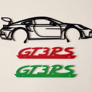 May include: Black outline of a sports car with a rear spoiler. Below are two felt cutouts of the text "GT3RS", one in red and one in green. The car outline is a side profile.