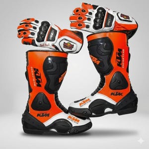 Könnte beinhalten: Ein Paar orangefarbene, schwarze und weiße KTM-Rennstiefel und passende Handschuhe. Die Stiefel und Handschuhe tragen das Red Bull-Logo und das KTM Racing Team-Branding. Die Stiefel haben eine weiße Sohle und schwarze Akzente.