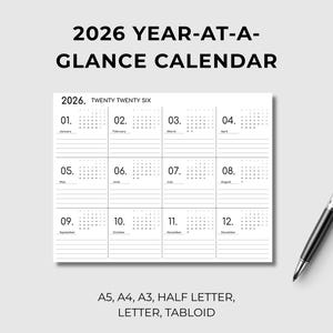 May include: A minimalist 2026 year-at-a-glance calendar with a simple layout. The calendar is white with black text, featuring monthly grids and the year 2026 at the top. A silver and black pen rests on the right. The text at the top reads "2026 YEAR-AT-A-GLANCE CALENDAR".