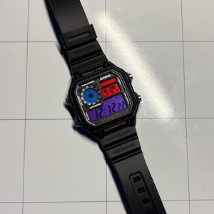 Puede incluir: Reloj digital Casio negro con esfera rectangular y correa negra. La esfera muestra la hora, la fecha y otras funciones en formato digital. El reloj tiene el texto "CASIO" e "ILLUMINATOR" impresos en la esfera.