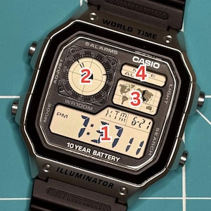 Puede incluir: Un reloj de pulsera digital plateado y negro con una esfera cuadrada que incluye el texto WORLD TIME, CASIO, 5 ALARMS, WR100M, 10 YEAR BATTERY e ILLUMINATOR. La pantalla muestra un mapa mundial, un reloj circular analógico y la hora.