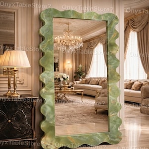 Könnte beinhalten: Ein großer, rechteckiger Spiegel mit einem wellenförmigen, hellgrünen Onyxrahmen. Der Spiegel spiegelt ein luxuriöses Wohnzimmer mit Kronleuchter, Sofas und Vorhängen wider. Das Logo Onyx Table Store? ist sichtbar.