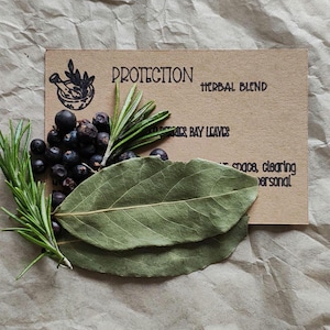 May include: A rectangular tan card with the text PROTECTION HERBAL BLEND, JUNIPER BERRIES, BAY LEAVES, and other text. The card is decorated with a cluster of dark purple juniper berries, green rosemary sprigs, and two large green bay leaves.