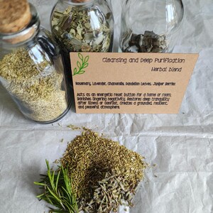 May include: Three clear glass jars with cork stoppers containing dried herbs, accompanied by a tan card labelled Cleansing and Deep Purification Herbal Blend, listing rosemary, lavender, chamomile, dandelion leaves, and juniper berries.