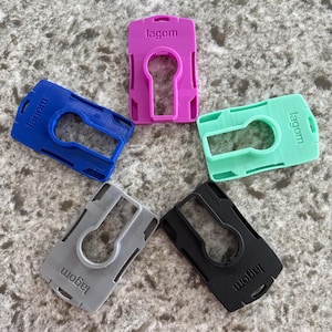 May include: Five colorful ID badge holders in blue, purple, green, gray, and black. Each holder has a keyhole-shaped opening and the word "lagom" printed on it. The holders are made of plastic.