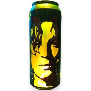 Peut inclure: Une canette verte et noire avec une silhouette jaune d'un visage. La canette a un éclat métallique et une surface texturée. Le haut de la canette est vert et le bas est noir.