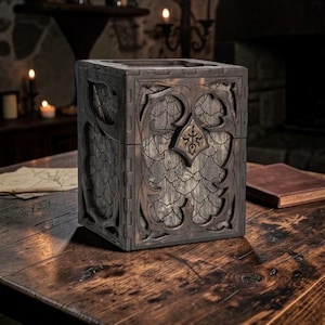 May include: A rectangular wooden box with a dark, weathered finish. The exterior features intricate laser-cut overlays with a scale-like pattern and a central diamond-shaped emblem. The construction shows visible interlocking joints at the edges.