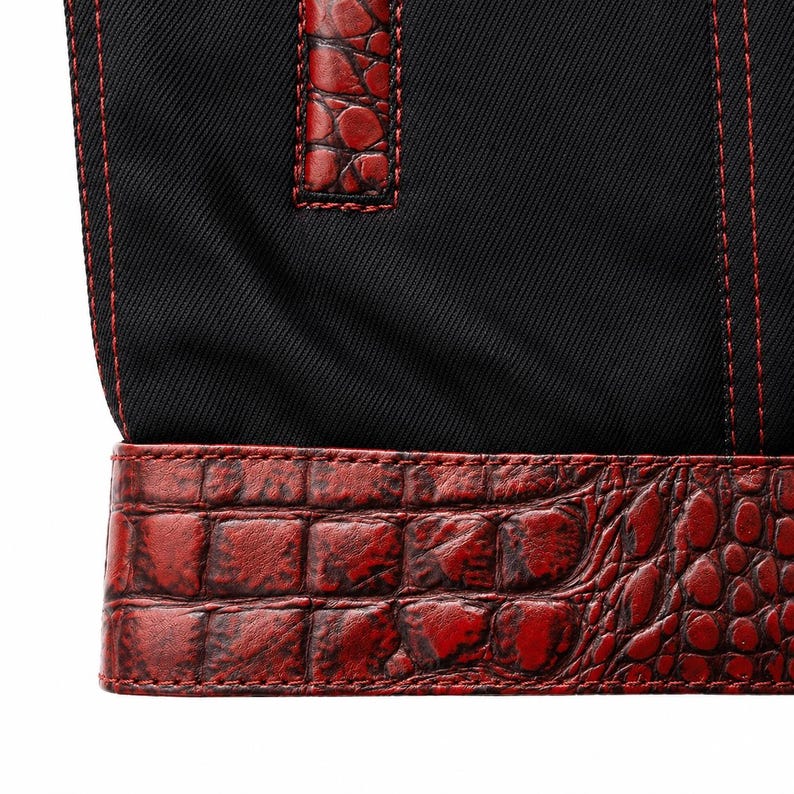 May include: Close-up of a black fabric bag with red stitching and a red crocodile-textured leather trim. The bag features a handle with matching red leather accents. The stitching is visible and adds a contrasting detail to the design.