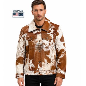 May include: A brown and white cowhide jacket with a classic collar, two chest pockets, and button closures. The jacket features a unique spotted pattern and a Moto Hide Custom logo.