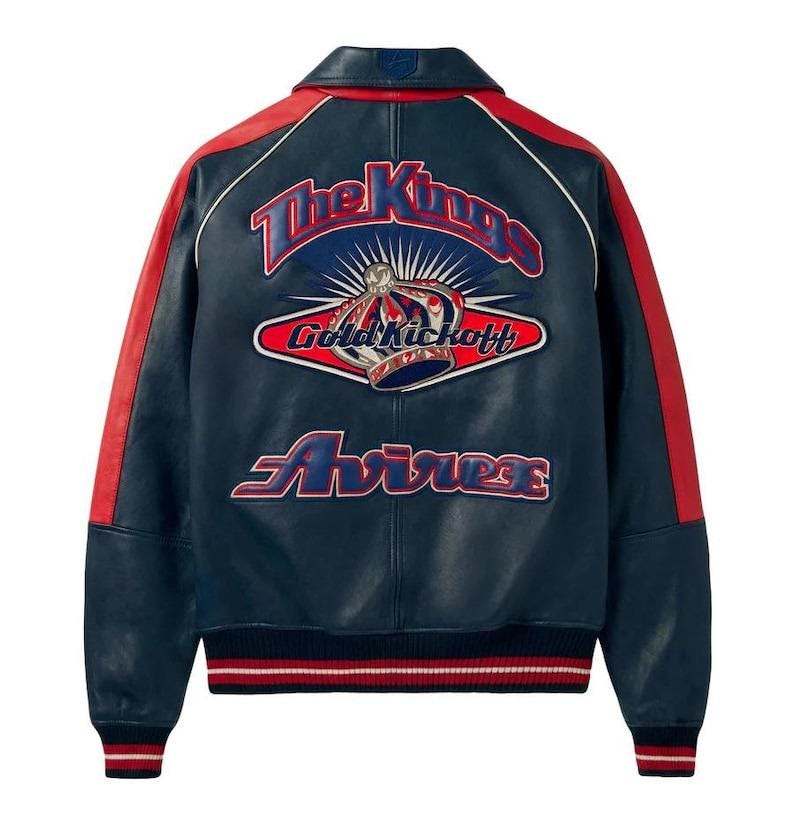 May include: Navy blue leather jacket with red accents on the shoulders and sleeves. The back features a large embroidered design with the text "The Kings", a crown, and "Gold Kickoff" and "Avirex". The jacket has a ribbed hem and cuffs.