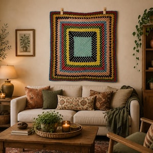 Puede incluir: Un tapiz de ganchillo cuadrado con bordes concéntricos en colores alternos que incluyen azul claro, negro, amarillo, rojo, verde y melocotón. La pieza textil muestra un patrón clásico de granny square y está colgada en una pared.