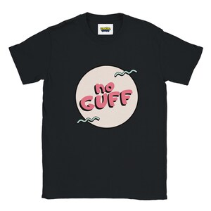 May include: A black short-sleeve t-shirt featuring a central graphic of a light beige circle containing the pink text "no GUFF" in a bold, rounded font. Two teal wavy lines are positioned above and below the text within the circle.