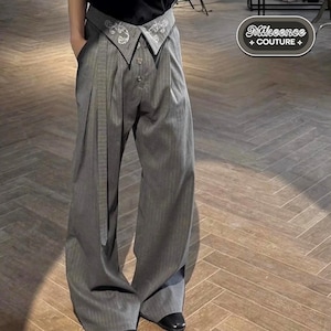 May include: Gray pinstripe trousers with a unique collar-like waistband featuring embroidered detailing. The pants have a wide-leg design, a button closure, and a matching belt. The brand name "Mikeence + COUTURE +" is visible in the upper right corner.