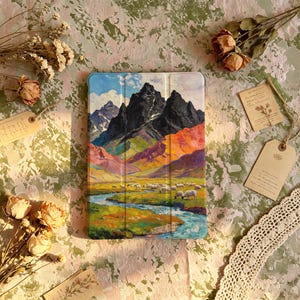 Puede incluir: Una funda rectangular para tableta con una pintura de paisaje vibrante que muestra montañas oscuras y escarpadas, colinas coloridas, un río azul serpenteante y un rebaño de ovejas blancas pastando en un prado bajo un cielo brillante.