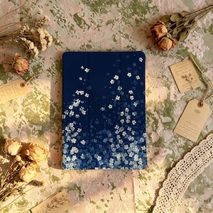 May include: A rectangular tablet case featuring a deep navy blue background adorned with a pattern of small, white, four-petaled flowers that appear to cascade from the top edge, becoming denser and more concentrated toward the bottom of the case.