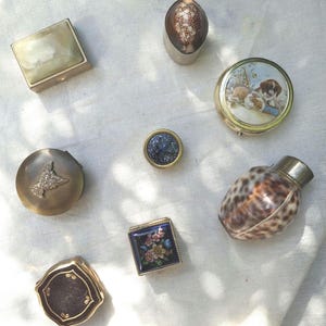 Peut inclure: Une collection de huit petites boîtes et contenants décoratifs, comprenant une boîte carrée en onyx, une boîte ronde en métal avec une illustration de chien, une boîte carrée en émail floral, une boîte en métal sombre avec un relief de chien.