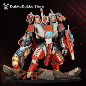 Op de afbeelding: Een miniatuur robotfiguur in rood, wit en donkergrijs pantser, met een groot kanon op de rechterarm, een schild aan de linkerarm en op de schouders gemonteerde raketwerpers. De tekst DakkaDakka.Store is zichtbaar bovenaan de afbeelding.