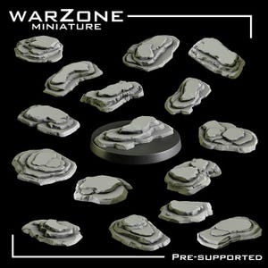 May include: A selection of grey miniature rock formations, suitable for tabletop gaming. The rocks are of various sizes and shapes, with layered textures. The image includes the text "WARZONE MINIATURE" and "PRE-SUPPORTED".