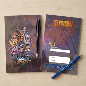 May include: Two notebooks with "Mobile Legends" graphics and a black and blue pen on a light wood surface. The notebooks feature colorful character illustrations and the game's logo. One notebook has a space for the name, class, and study.