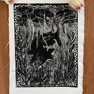 Könnte beinhalten: Ein Schwarz-Weiß-Linolschnitt auf einem weißen Stoffquadrat. Der Druck zeigt eine stilisierte Waldszene mit hohen Bäumen, Blättern und einer dunklen, silhouettenartigen Kreatur. Der Stoff hat einen rohen, unfertigen Rand. Getrocknete Blumen sind oben platziert.