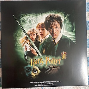 Może przedstawiać: Kwadratowa okładka albumu "Harry Potter i Komnata Tajemnic" z głównymi postaciami. Tytuł jest złoty, z tytułem filmu i tekstem "Original Motion Picture Soundtrack" na dole.