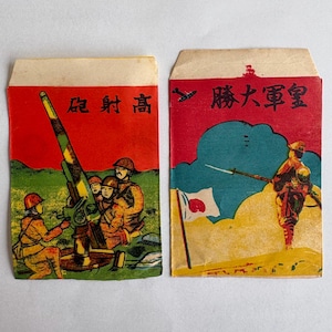 以下が含まれることがあります： 兵士のヴィンテージイラストが描かれた2枚の長方形の紙製封筒。左側の封筒には高射砲を操作する兵士と「砲射高」の文字があり、右側の封筒には旗を持つ兵士と「勝大軍皇」の文字が描かれています。