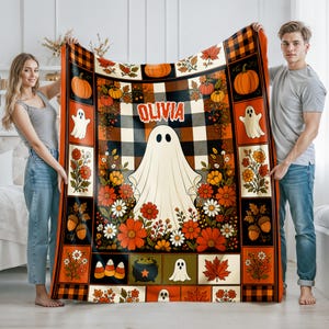 May include: A rectangular throw blanket featuring a black and white buffalo plaid background with a large central ghost and the name OLIVIA in orange text. The border includes pumpkins, ghosts, autumn flowers, acorns, and maple leaves.