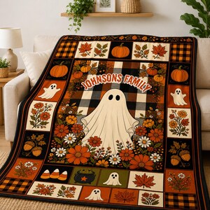 May include: A rectangular throw blanket featuring a grid pattern with a central ghost illustration and the text "JOHNSONS FAMILY". The design includes orange pumpkins, autumn leaves, white ghosts, flowers, acorns, and candy corn on a plaid background.