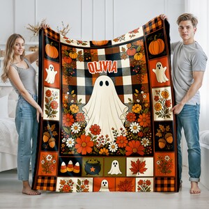 May include: A rectangular throw blanket featuring a central white ghost graphic above the name OLIVIA, surrounded by a patchwork pattern of orange and black buffalo plaid, pumpkins, autumn flowers, acorns, candy corn, and maple leaves.