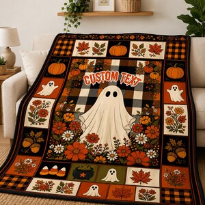 May include: A rectangular throw blanket featuring a central ghost illustration surrounded by autumn flowers, pumpkins, and acorns. The design includes a black and white buffalo plaid background, orange accents, and the text CUSTOM TEXT in a stylized font.