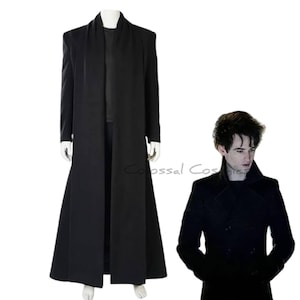 Puede incluir: Un abrigo largo negro con cuello alto y diseño fluido. El abrigo se muestra en un maniquí. Una persona lleva un abrigo negro con un diseño similar. La imagen está sobre un fondo blanco.
