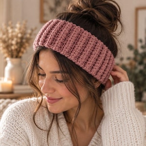 May include: A dusty rose crochet headband featuring a thick, ribbed texture. The accessory is crafted with a consistent vertical stitch pattern that wraps around the head, providing a structured look with a soft, matte yarn finish.
