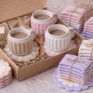 May include: A gift set featuring three mugs with knitted cozies, a wooden spoon, and daisy-shaped coasters. The set includes stacks of square, knitted coasters in various pastel colors, all presented in a cardboard box.