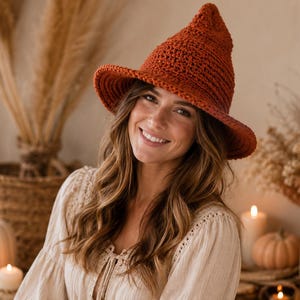 May include: A rust-colored crochet witch hat with a wide brim. The hat is the focal point of the image, with a pointed crown and a textured appearance. The hat is likely handmade and suitable for Halloween or costume events.