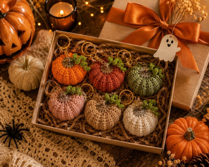 Puede incluir: Una caja con seis llaveros de calabaza de ganchillo en varios colores: naranja, rojo, verde, rosa, beige y blanco. Cada calabaza tiene un tallo verde y un llavero dorado. La caja est&aacute; junto a una caja de regalo con un lazo.