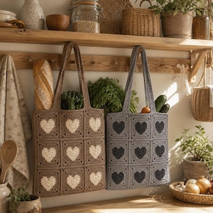 May include: Two crochet tote bags, one brown with white hearts and the other gray with dark gray hearts, hang on a wooden rack. Each bag is filled with groceries, including bread, vegetables, and fruit. The bags are part of a kitchen decor.