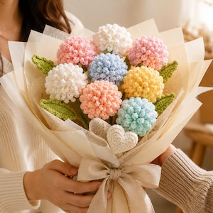 May include: A bouquet of crocheted flowers in pastel shades of pink, blue, yellow, and white, featuring textured spherical blooms and green crocheted leaves. The arrangement is wrapped in beige paper with a matching ribbon and a small crocheted heart.