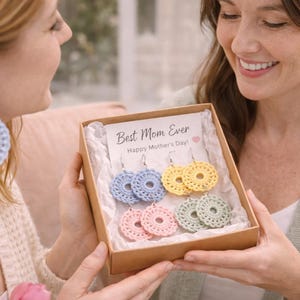 May include: A gift box containing several pairs of handmade crochet earrings in pastel colours: blue, yellow, pink, and green. The box includes a card that reads "Best Mom Ever Happy Mother's Day!" The earrings are circular with a detailed openwork design.