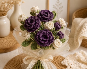 May include: A handcrafted bouquet of crochet flowers. The bouquet features deep purple and cream-colored roses with green leaves, wrapped in sheer white fabric and tied with a cream ribbon. The flowers are arranged to resemble a natural bouquet.